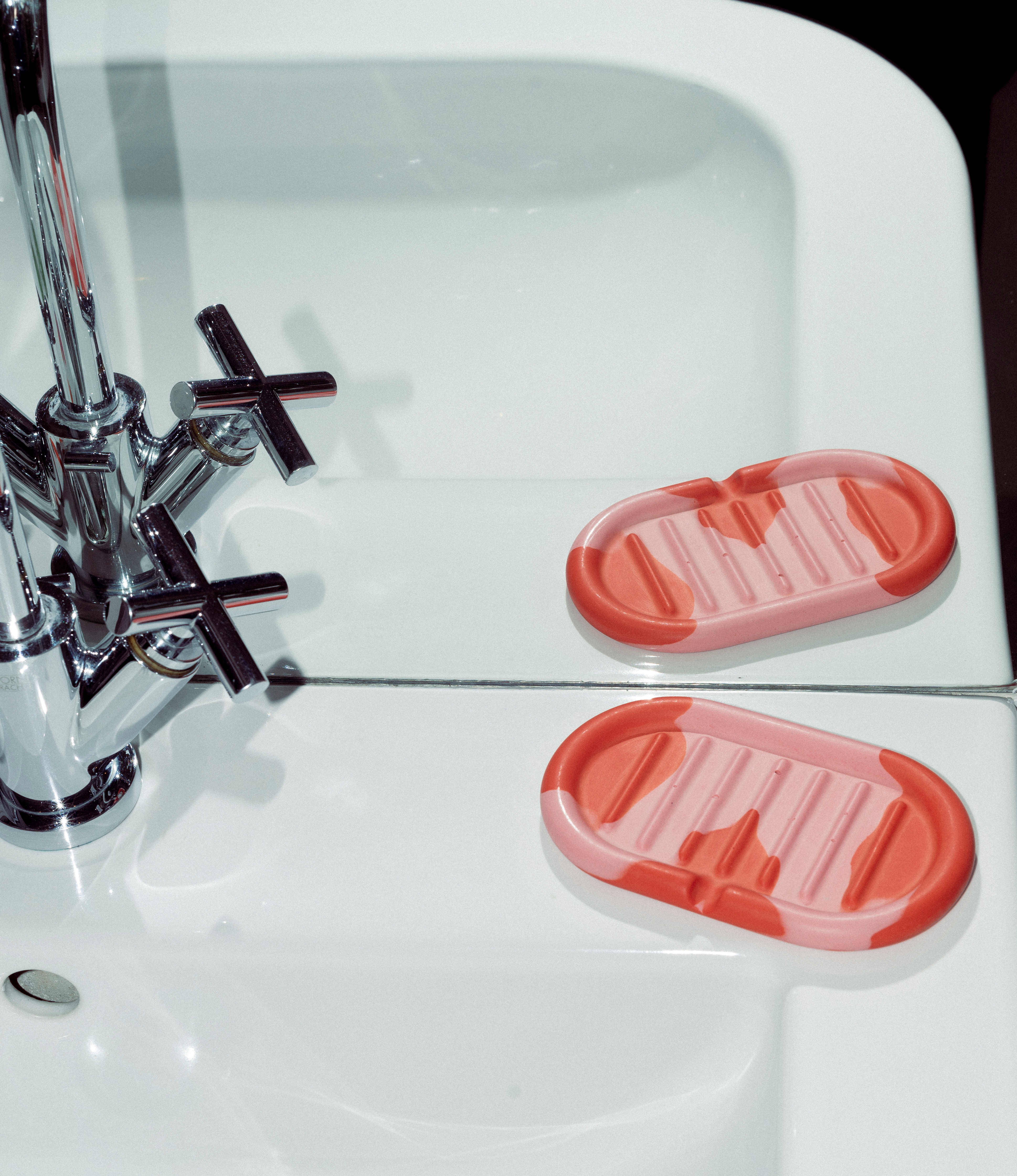 Soap holder from Gritful Homeware coming in the color pairing rose and orange, being spotted on a white bathroom sink. 